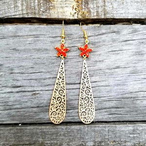 May include: A pair of gold-colored earrings with a red flower design at the top. The earrings have a long, teardrop shape with a detailed, openwork scroll pattern. The earrings hang from gold-colored hooks.