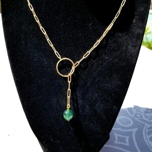 May include: A gold chain necklace with a green gemstone pendant and a gold circle charm. The necklace is on a black background.