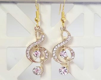Op de afbeelding: Gouden oorbellen met een treble clef-ontwerp, versierd met heldere en roze strass.