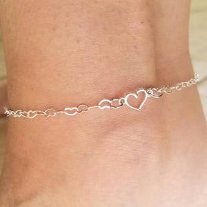 May include: A silver anklet with a heart charm and a delicate chain made of linked hearts.