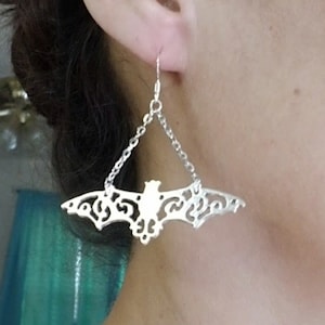 Op de afbeelding: Zilveren oorhangers met een delicaat, ingewikkeld vleermuisontwerp. De vleermuis hangt aan een zilveren ketting.