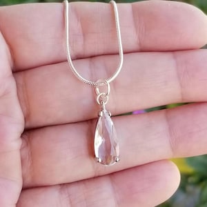 May include: A silver chain necklace with a teardrop-shaped pendant featuring a clear, faceted gemstone.