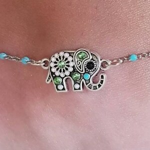 Op de afbeelding: Een enkelbandje met een zilveren olifantbedel. De olifant is versierd met groene, witte en zwarte strass steentjes.