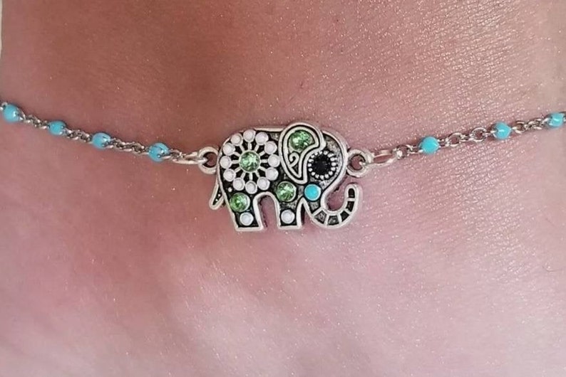 Op de afbeelding: Een enkelbandje met een zilveren olifantbedel. De olifant is versierd met groene, witte en zwarte strass steentjes.