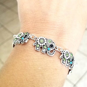 Op de afbeelding: Zilveren armband met vier olifantenbedels. Elke olifantenbedel is versierd met groene en blauwe strasssteentjes.