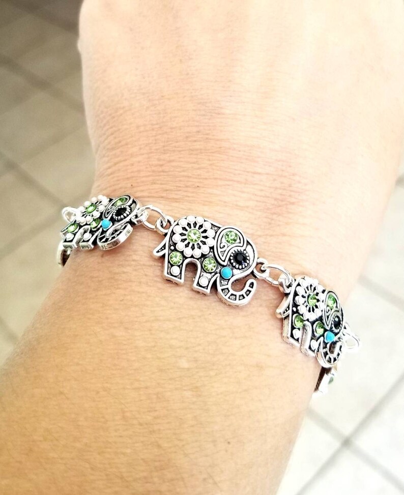 Op de afbeelding: Zilveren armband met vier olifantenbedels. Elke olifantenbedel is versierd met groene en blauwe strasssteentjes.