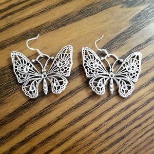 May include: A pair of silver butterfly earrings with clear rhinestone accents. The earrings have a delicate, intricate design.