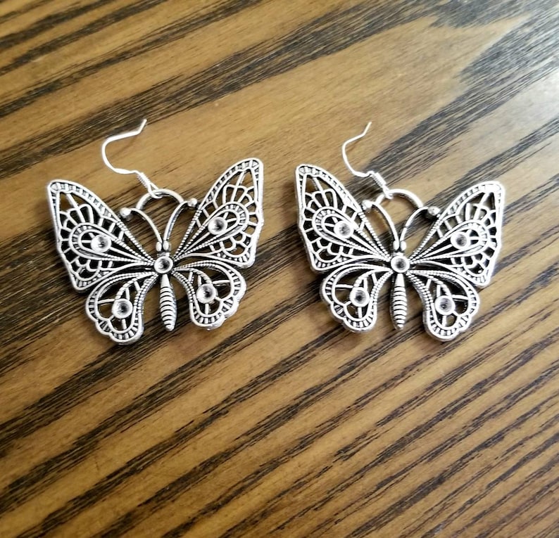 May include: A pair of silver butterfly earrings with clear rhinestone accents. The earrings have a delicate, intricate design.
