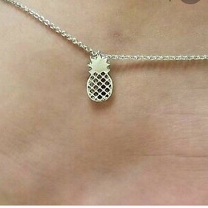 May include: A silver ankle bracelet with a pineapple charm.