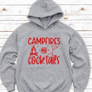 May include: Gray hooded sweatshirt with the text "Campfires and Cocktails" in red lettering. The text is stylized with a campfire graphic and a cocktail glass.