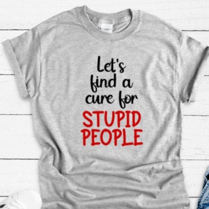 May include: A light gray t-shirt with the text "Let's find a cure for STUPID PEOPLE" in black and red. The shirt has a crew neck and short sleeves, and is made of a soft material.