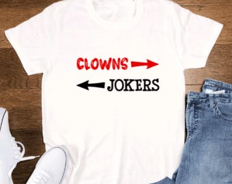 Puede incluir: Camiseta blanca con texto negro y rojo que dice "Clowns -> Jokers" con flechas apuntando en direcciones opuestas.