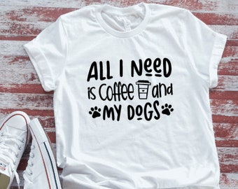 May include: White t-shirt with black text that reads "All I Need is Coffee and My Dogs" with a coffee cup icon and paw prints.