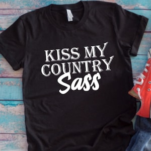 May include: Black t-shirt with white text that reads "Kiss My Country Sass".