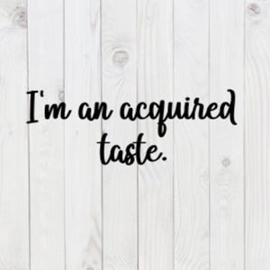 Pode incluir: Texto preto sobre fundo branco de madeira. A frase "I'm an acquired taste" está escrita em itálico. O fundo é composto por tábuas de madeira verticais.
