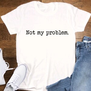May include: White t-shirt with the text "Not my problem." printed in black.