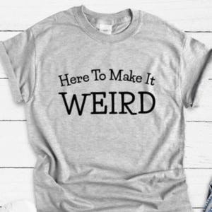 May include: Gray t-shirt with black text that reads "Here To Make It WEIRD".
