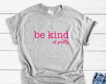 May include: A heather gray t-shirt with the phrase "be kind of petty" printed in pink. The shirt has short sleeves and a crew neck. The text is in a bold, sans-serif font with the word "petty" in a cursive font.