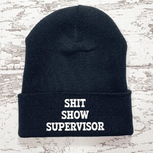 May include: Black beanie with white text that reads "SHIT SHOW SUPERVISOR".