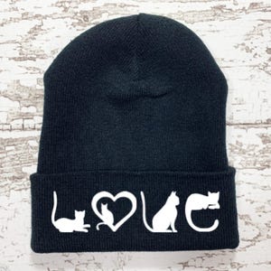 May include: Black knit beanie with a white graphic of cats forming the word "LOVE" on the cuff.