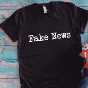 May include: Black t-shirt with white text that reads "Fake News".