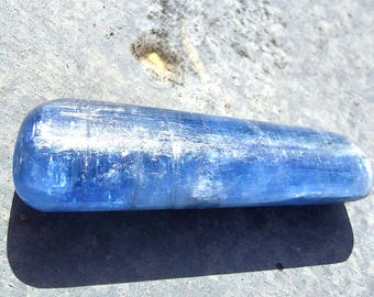May include: A smooth, polished blue aquamarine crystal in the shape of a long, rounded cylinder. The crystal has a light blue color and a slightly iridescent sheen.