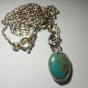 Puede incluir: Un collar de cadena de plata con un colgante de turquesa. El colgante tiene forma ovalada y tiene un engaste de plata.