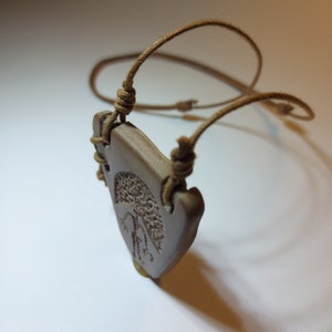 May include: A brown leather cord necklace with a ceramic pendant featuring a detailed tree design.
