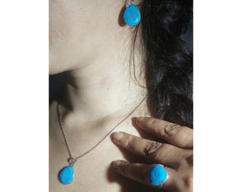 May include: A silver necklace with a turquoise teardrop pendant and matching earrings. The necklace and earrings are on a person's neck and ear.
