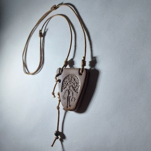 May include: A brown leather cord necklace with a brown ceramic pendant featuring a tree design. The pendant is shaped like a triangle.