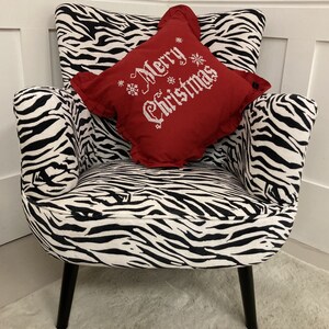 May include: A black and white zebra patterned armchair with a red pillow that says "Merry Christmas" in white embroidery.