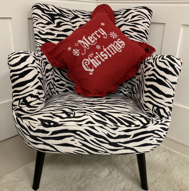 May include: A black and white zebra patterned armchair with a red pillow that says "Merry Christmas" in white embroidery.
