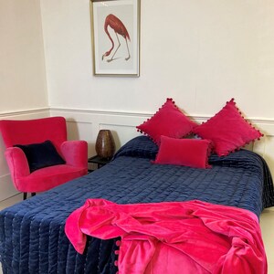 Pu&ograve; includere: Un copriletto trapuntato blu navy con una coperta in velluto rosa e cuscini in velluto rosa. Il copriletto ha un motivo trapuntato sottile e i cuscini hanno dei pompon intorno ai bordi.