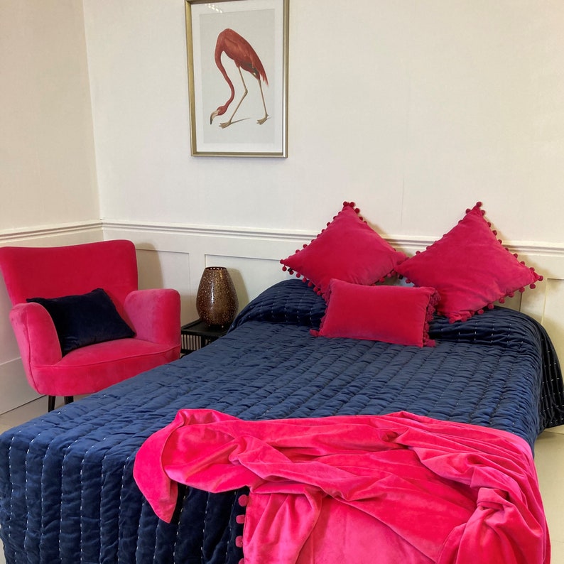 Pu&ograve; includere: Un copriletto trapuntato blu navy con una coperta in velluto rosa e cuscini in velluto rosa. Il copriletto ha un motivo trapuntato sottile e i cuscini hanno dei pompon intorno ai bordi.