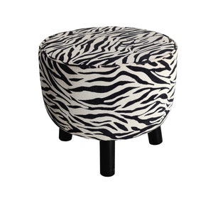 May include: A round, black and white zebra print ottoman with three black wooden legs.