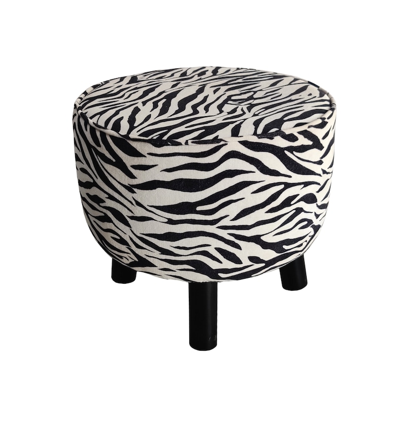 May include: A round, black and white zebra print ottoman with three black wooden legs.
