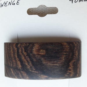 May include: A close-up of a dark brown wood veneer sample labeled "WENGE". The wood grain is visible and has a dark brown and black color.