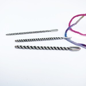 May include: Three silver crochet needles with twisted metal shafts and eye loops. The needles are arranged in order of size, with the largest needle at the bottom and the smallest needle at the top.