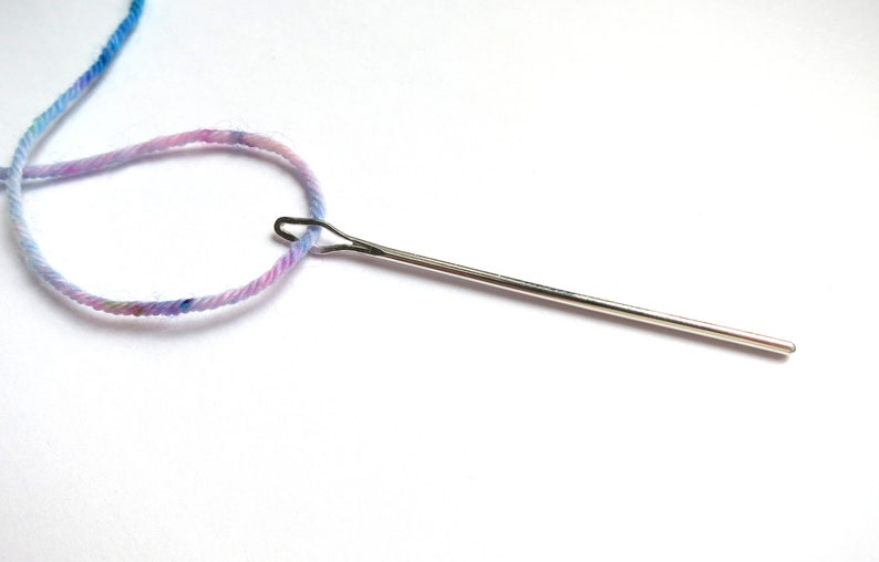 May include: A close-up of a needle threaded with light blue and pink yarn.