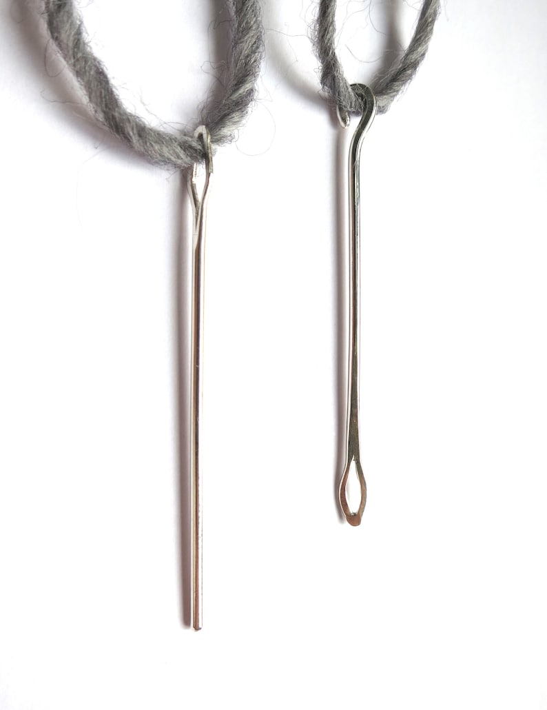 May include: Two silver yarn needles with grey yarn attached to the top of each needle.