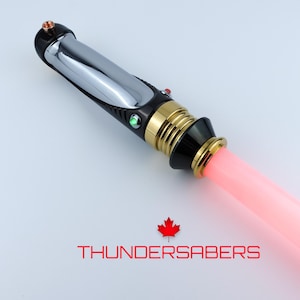 May include: A lightsaber with a chrome and black handle, gold accents, and a glowing pink blade. The handle has a red and green button. The text "THUNDERSABERS" is displayed below the lightsaber with a red maple leaf.