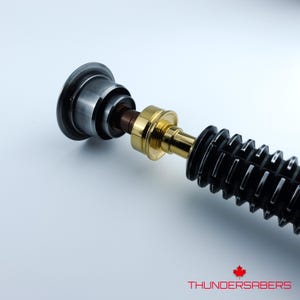 May include: A lightsaber prop with a black, gold, and silver design. The hilt has a ribbed texture and metallic accents. The text "THUNDERSABERS" is visible at the bottom.