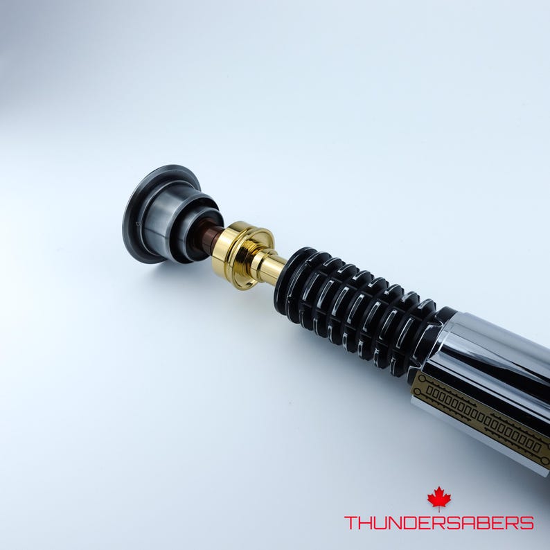 May include: A lightsaber in black, silver, and gold. The hilt features a ribbed black grip, a gold midsection, and a silver blade emitter. The text "THUNDERSABERS" is visible at the bottom of the image.