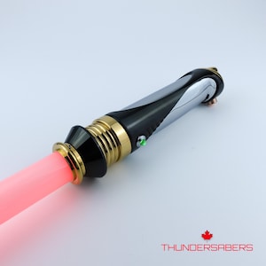 Puede incluir: Un sable de luz con una hoja roja, empu&ntilde;adura negra y plateada, y detalles dorados. El mango tiene un bot&oacute;n verde y est&aacute; marcado con "THUNDERSABERS" y una hoja de arce.