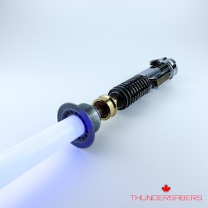 May include: A lightsaber with a white blade and a black and gold hilt. The hilt has a ribbed design and a circular emitter. The blade glows with a soft white light, transitioning to blue at the base. The logo "THUNDERSABERS" is visible.