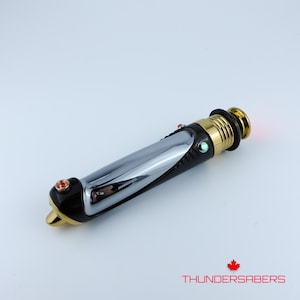 Puede incluir: Un sable de luz cromado y negro con detalles dorados. El mango presenta un acabado cromado pulido, secciones de agarre negras y detalles dorados. Tiene botones iluminados en rojo y verde. El texto "THUNDERSABERS" es visible.