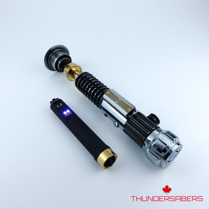 May include: A detailed lightsaber prop with a black, silver, and gold finish. The hilt features intricate detailing, and a separate black control unit with blue lights is included. The Thundersabers logo is visible in the bottom right corner.