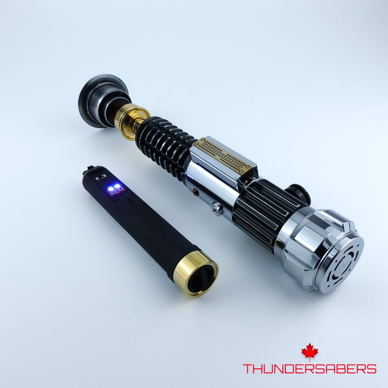 May include: A silver, black, and gold lightsaber with a separate black and gold hilt. The lightsaber has intricate detailing and a metallic finish. The hilt has a digital display. The logo "THUNDERSABERS" is in the bottom right corner.