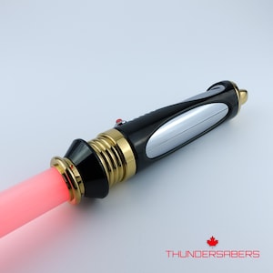 Puede incluir: Un sable de luz negro y dorado con una hoja roja. El mango presenta detalles dorados, un panel plateado y un bot&oacute;n rojo. El texto "THUNDERSABERS" est&aacute; en la parte inferior.