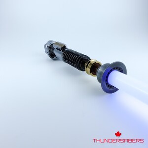 May include: A lightsaber with a silver and black hilt, gold detailing, and a bright white and blue blade. The text "THUNDERSABERS" is visible at the bottom of the image.
